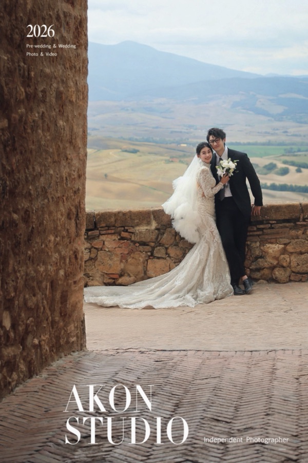 Couple leaning on the stone parapet of Pienza's terrace, the rolling hills of the Val d'Orcia behind them